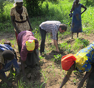 Drew helps to weed the garden of Nelly Okello